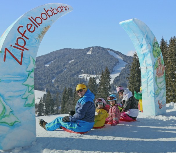 Mann fährt mit Kindern Zipflbob am Zipflbobbahn